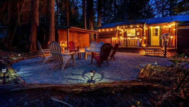 Una baita con patio in ghiaia, sedute all'aperto e un portico con luci decorative.