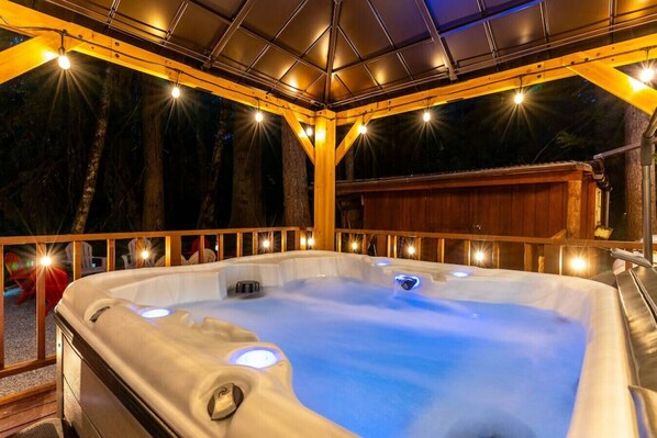 Een hottub met een houten terras en leuningen, omgeven door bomen.