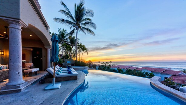 A poolside area with lounge chairs and a view of the ocean at sunset. - 5BR Luxury Home in Villas del Mar (Los Cabos)