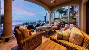 A sunlit outdoor seating area with wicker furniture, a wooden table, and a view of the ocean. - 5BR Luxury Home in Villas del Mar (Los Cabos)