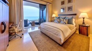 Une chambre d’hôtel avec un grand lit, deux lampes de chevet, une vue sur la mer et un bureau avec une chaise.
