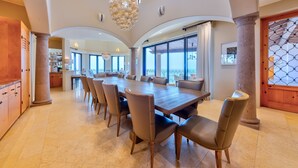Un vaste espace dédié à la salle à manger, avec une grande table en bois et des chaises modernes, le tout agrémenté de grandes fenêtres et d’un lustre décoratif.