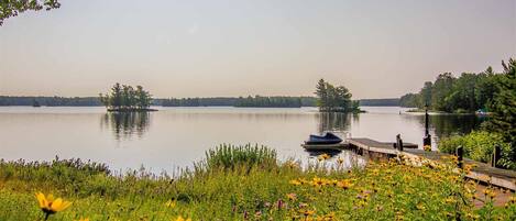 Un lago con un muelle y un bote, rodeado de vegetación y flores.