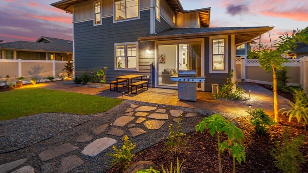 Une maison à deux étages avec un chemin de pierre menant à un patio, un barbecue et un petit jardin.
