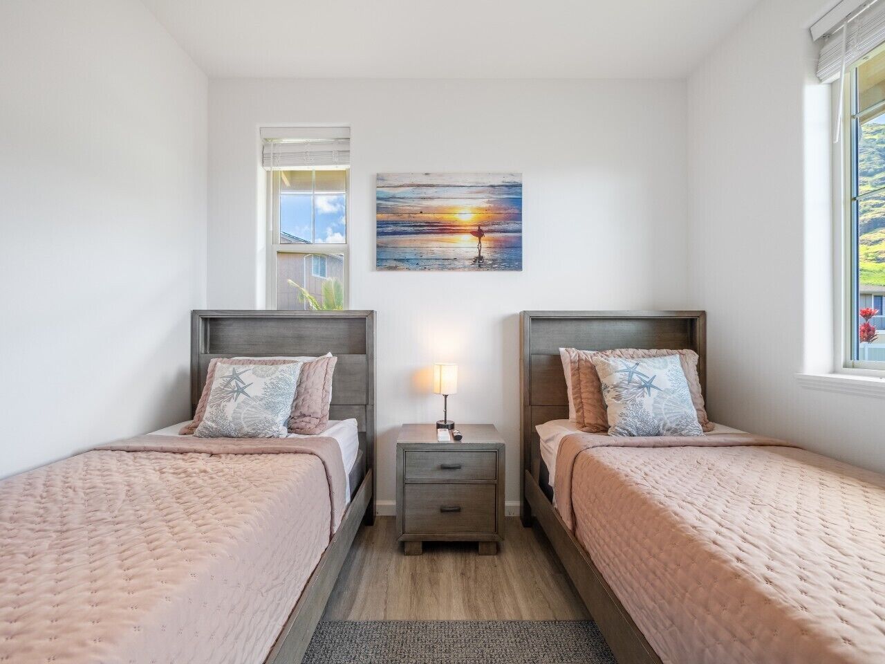 A bedroom with two beds, a nightstand, a lamp, and a painting on the wall.