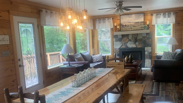 A wooden cabin interior with a long dining table, benches, a fireplace, and large windows. - Blue Sky Relaxation Retreat! (Gatlinburg)