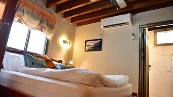 A hotel room with a bed, a ceiling fan, an air conditioning unit, a framed picture on the wall, and a door leading to a bathroom.