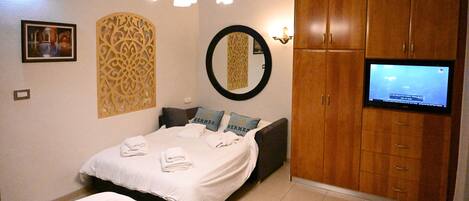 A bedroom with a bed, a television, wooden cabinets, a mirror, and decorative wall panels.