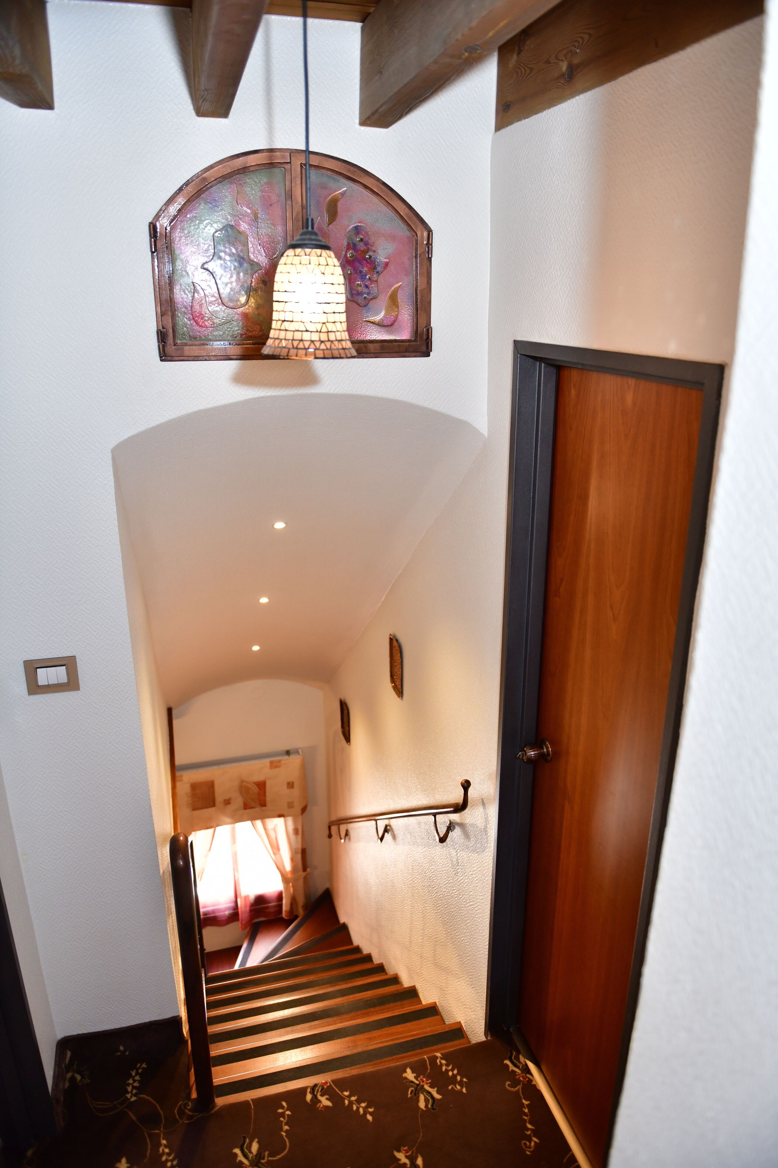 A staircase with a wooden handrail, a door with a dark frame, and a wall-mounted light fixture.