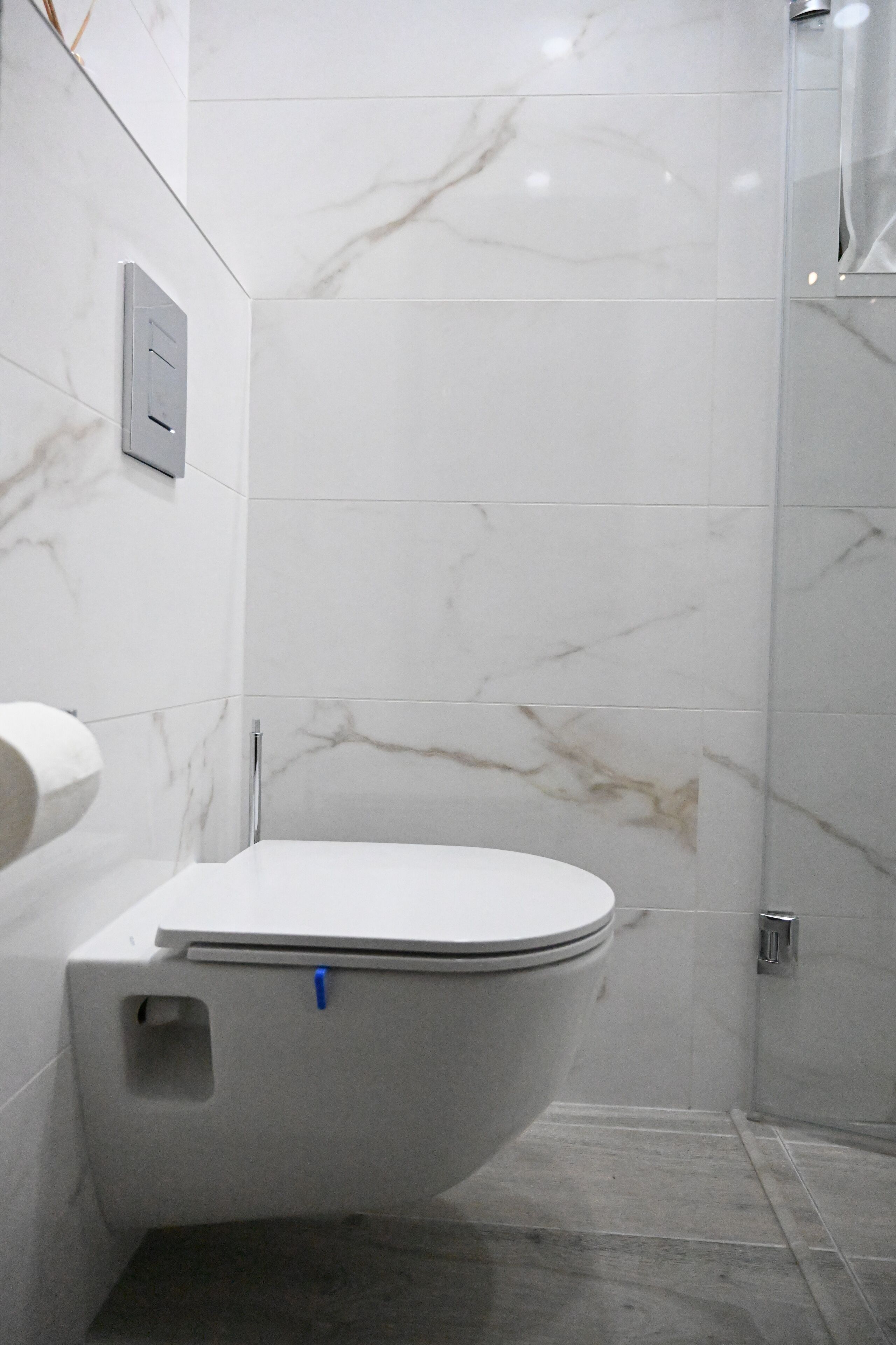 Un baño moderno con inodoro, azulejos de mármol y cabina de ducha de vidrio.