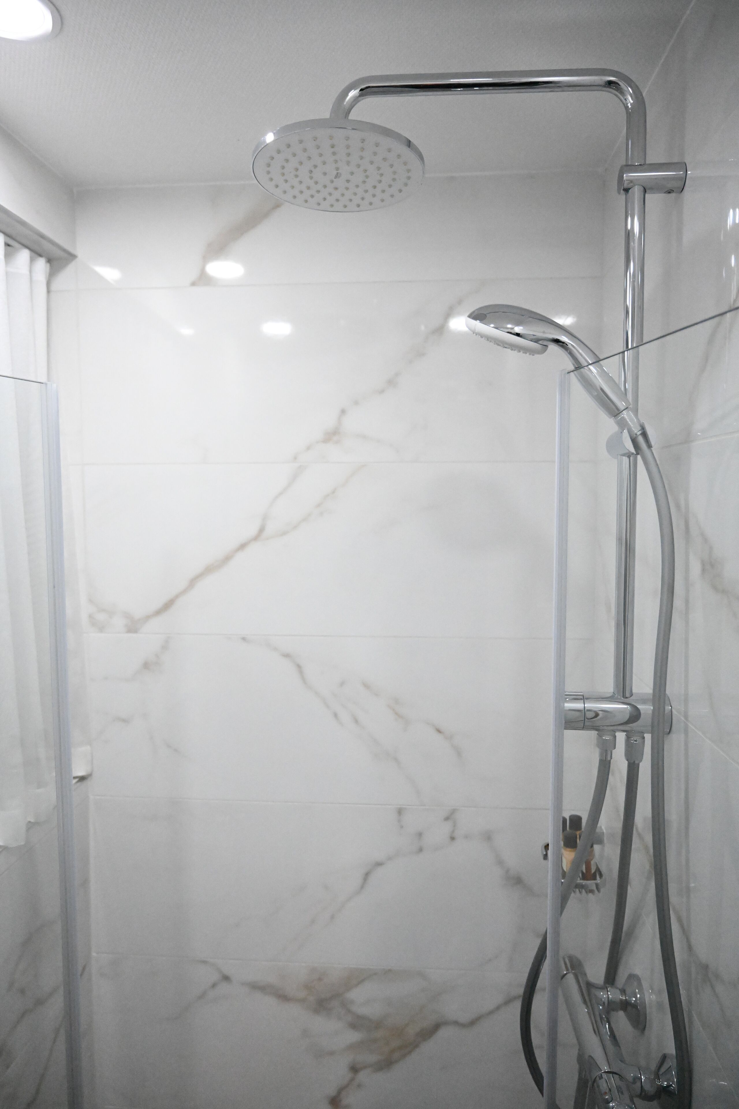 Una ducha moderna con cabezal de ducha manual y grifo empotrado en una pared con azulejos de mármol.