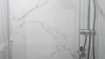 Una ducha moderna con cabezal de ducha manual y grifo empotrado en una pared con azulejos de mármol.