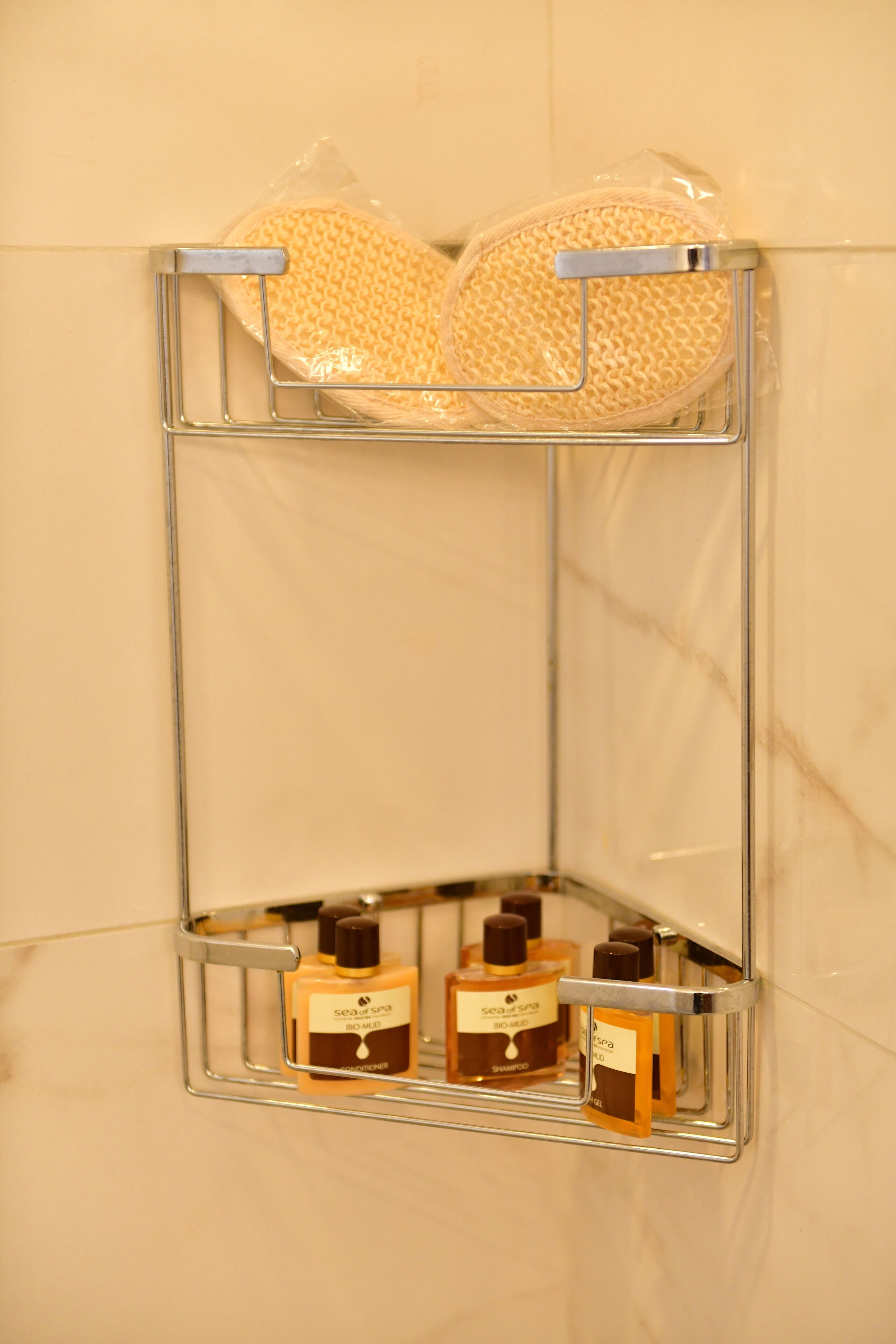 A bathroom with a shower area, a towel rack, and three bottles of shampoo and conditioner.