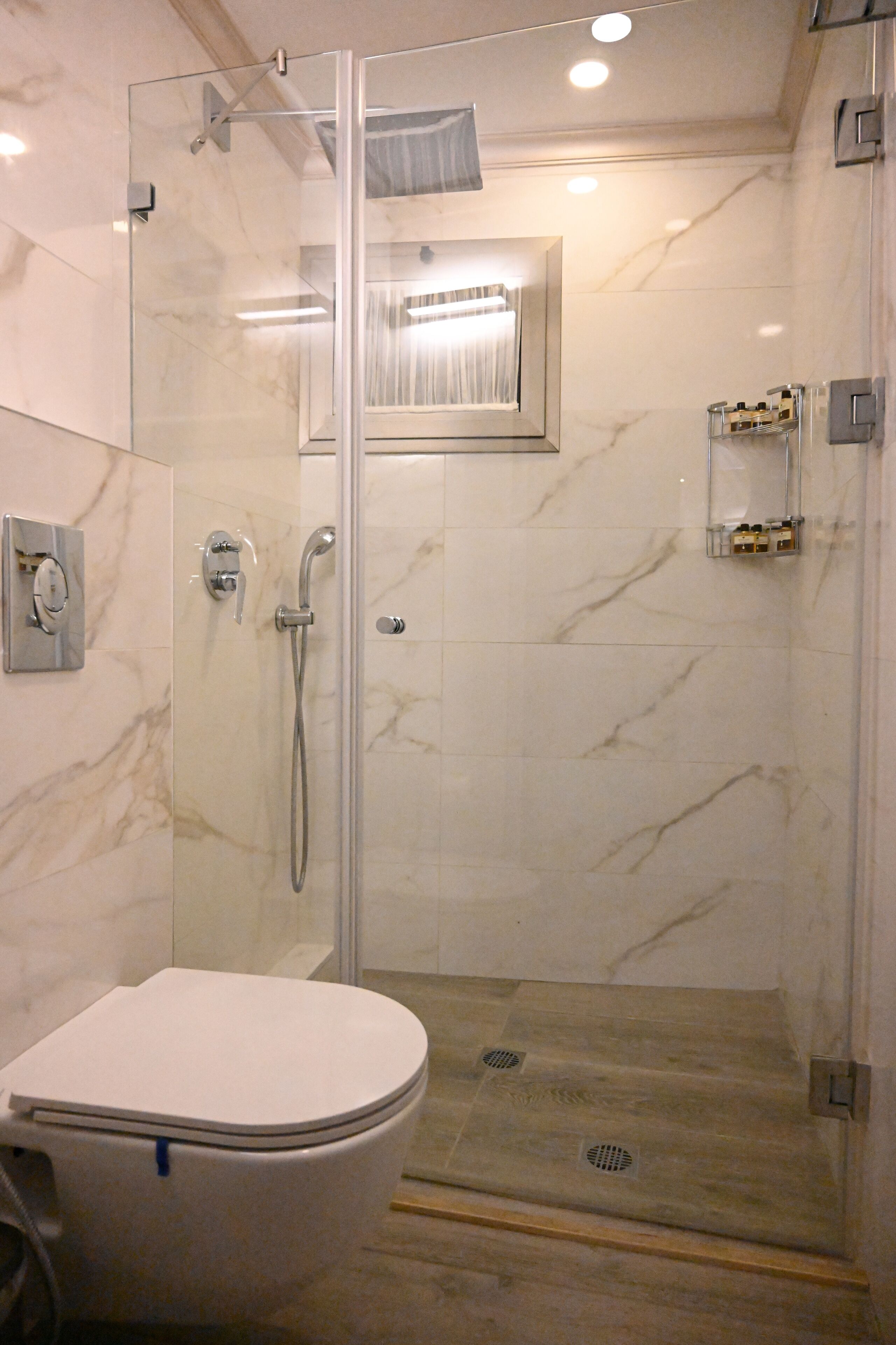 A modern bathroom with a glass-enclosed shower, a toilet, and a marble-tiled floor.