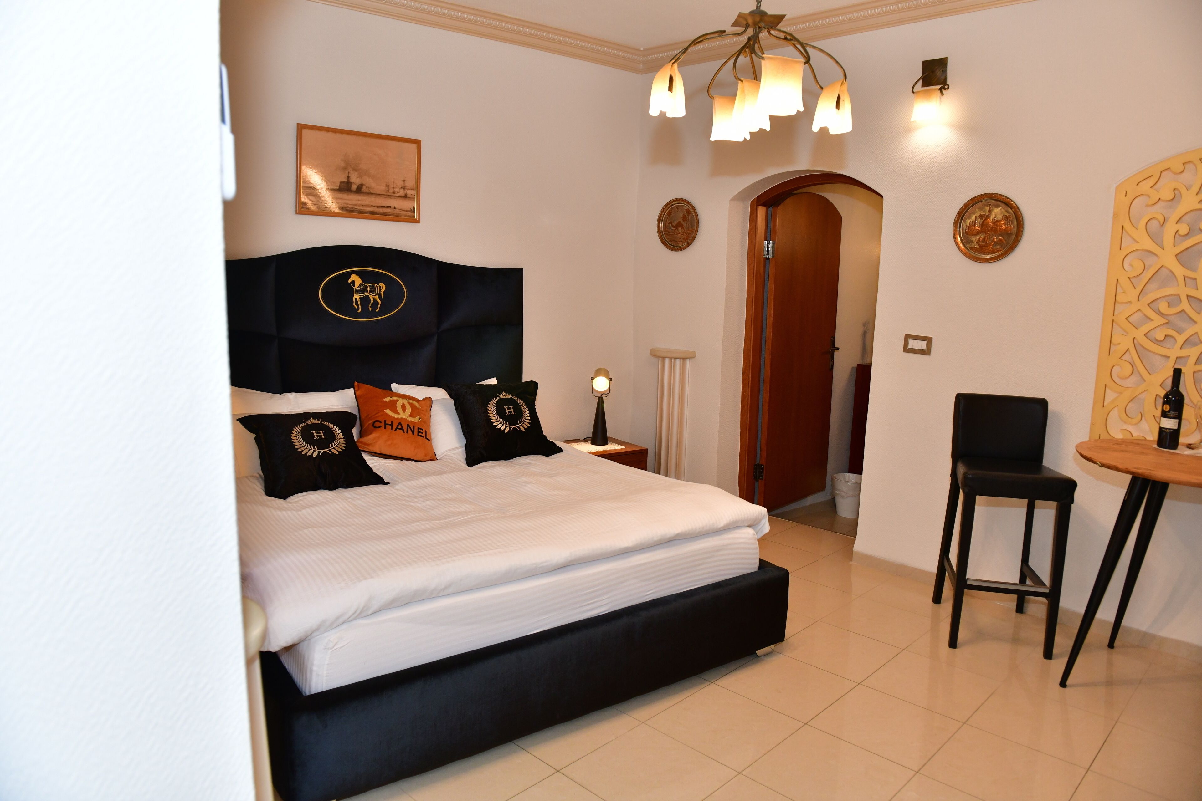 Une chambre d’hôtel avec un grand lit, un bureau et une chaise. Il y a une porte qui donne sur une autre pièce et un mur orné d’assiettes décoratives.