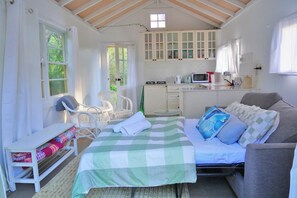 A cozy bedroom with a bed, a chair, a small table, and a kitchenette area with a microwave and cabinets.