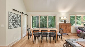 A dining area with a large wooden table and six chairs, a decorative metal wall piece, a cabinet with a mirror, and a sofa.