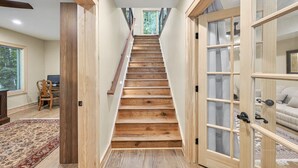 A wooden staircase leading to a second floor with a view of greenery outside.