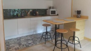 Una cocina moderna con armarios blancos, un microondas y una cafetera. Hay tres taburetes y una mesa de madera con individuales.