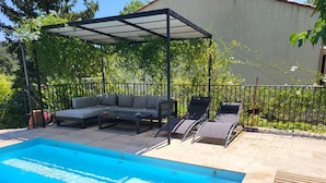 En have med swimmingpool, overdækket siddeområde og en indhegnet have.