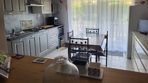 Et moderne køkken med lysegrå skabe, en kaffemaskine og et spiseområde med bord og stole.