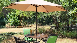 En udendørs terrasse med et rundt bord, fire stole og en stor parasol.