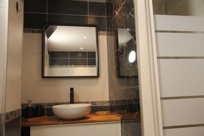 A bathroom with a white sink, black and white tiles, a mirror, and a wooden countertop. - Gite Rental in the Var (Le Thoronet)