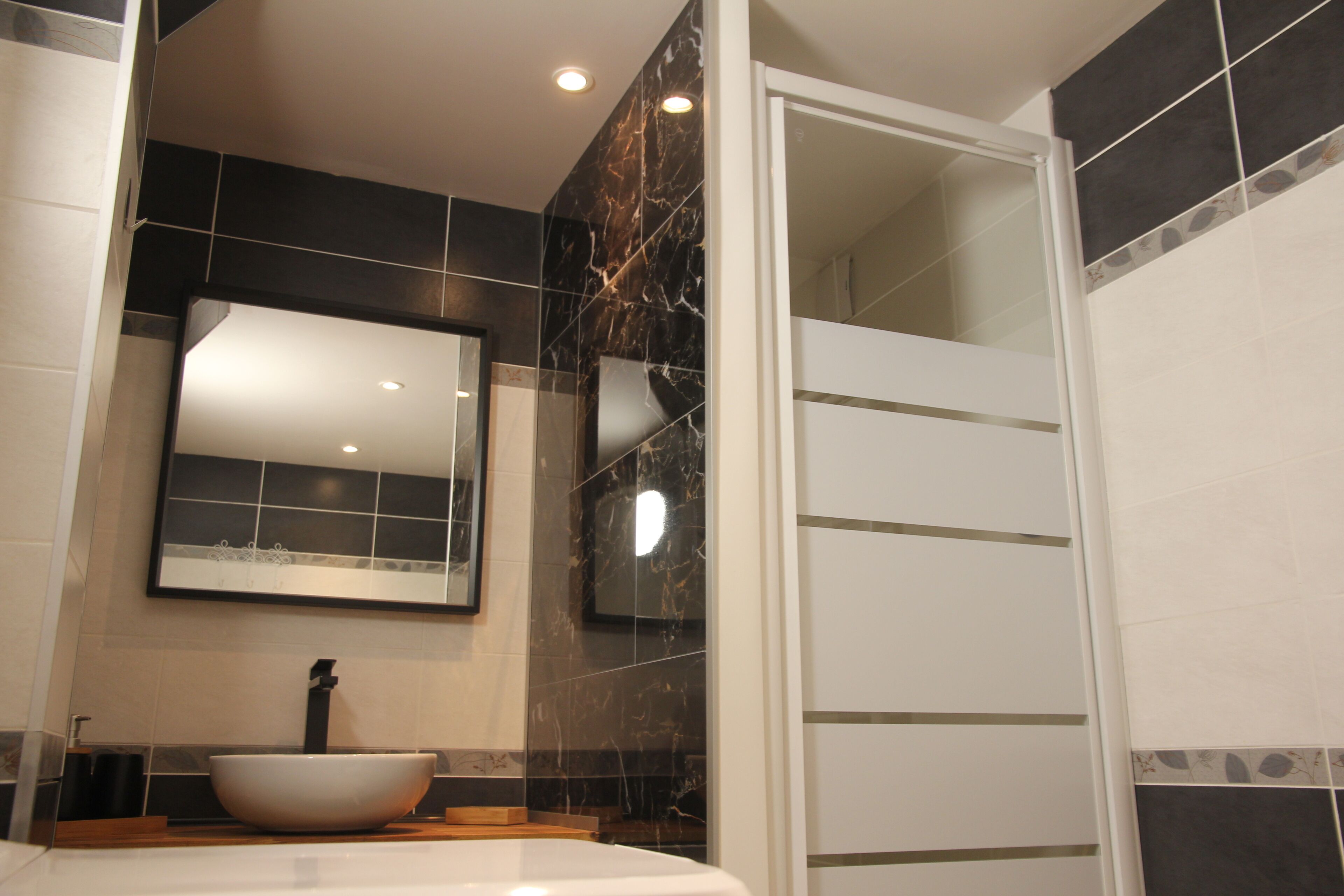 A modern bathroom with a large mirror, a vessel sink, and a shower area.