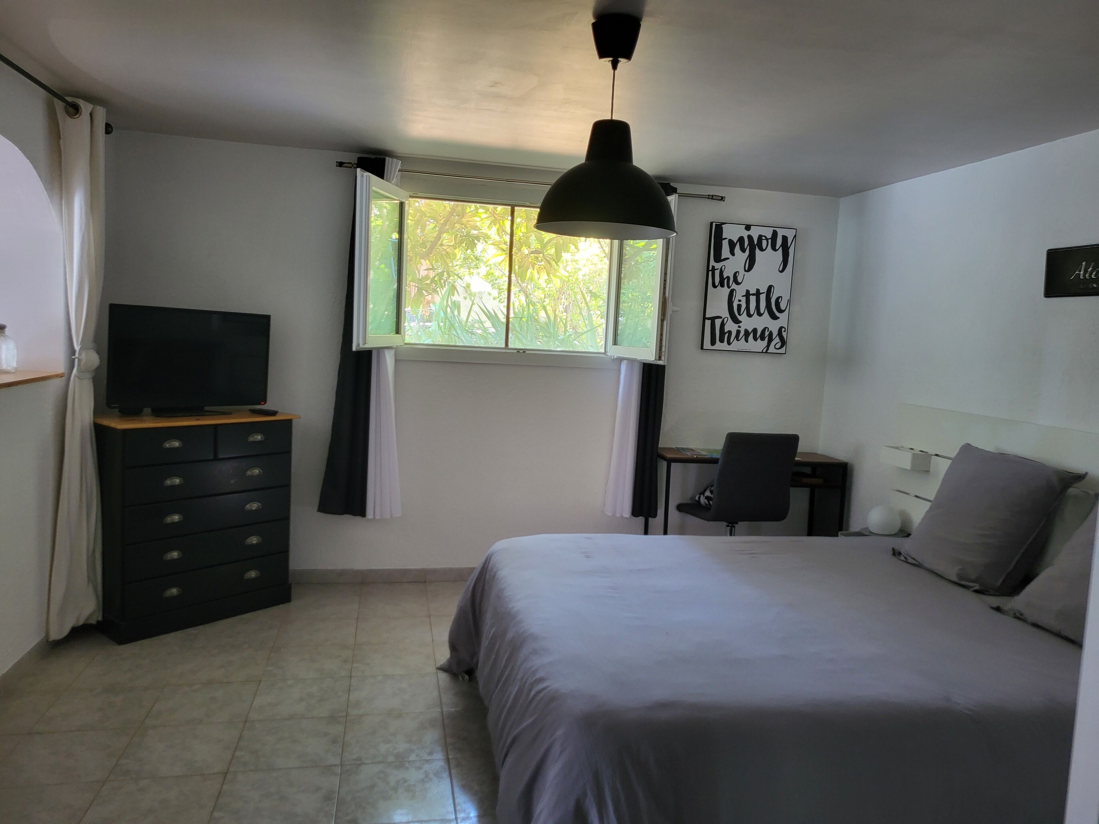 A bedroom with a bed, a desk, a chair, a dresser, a television, and a window with curtains.