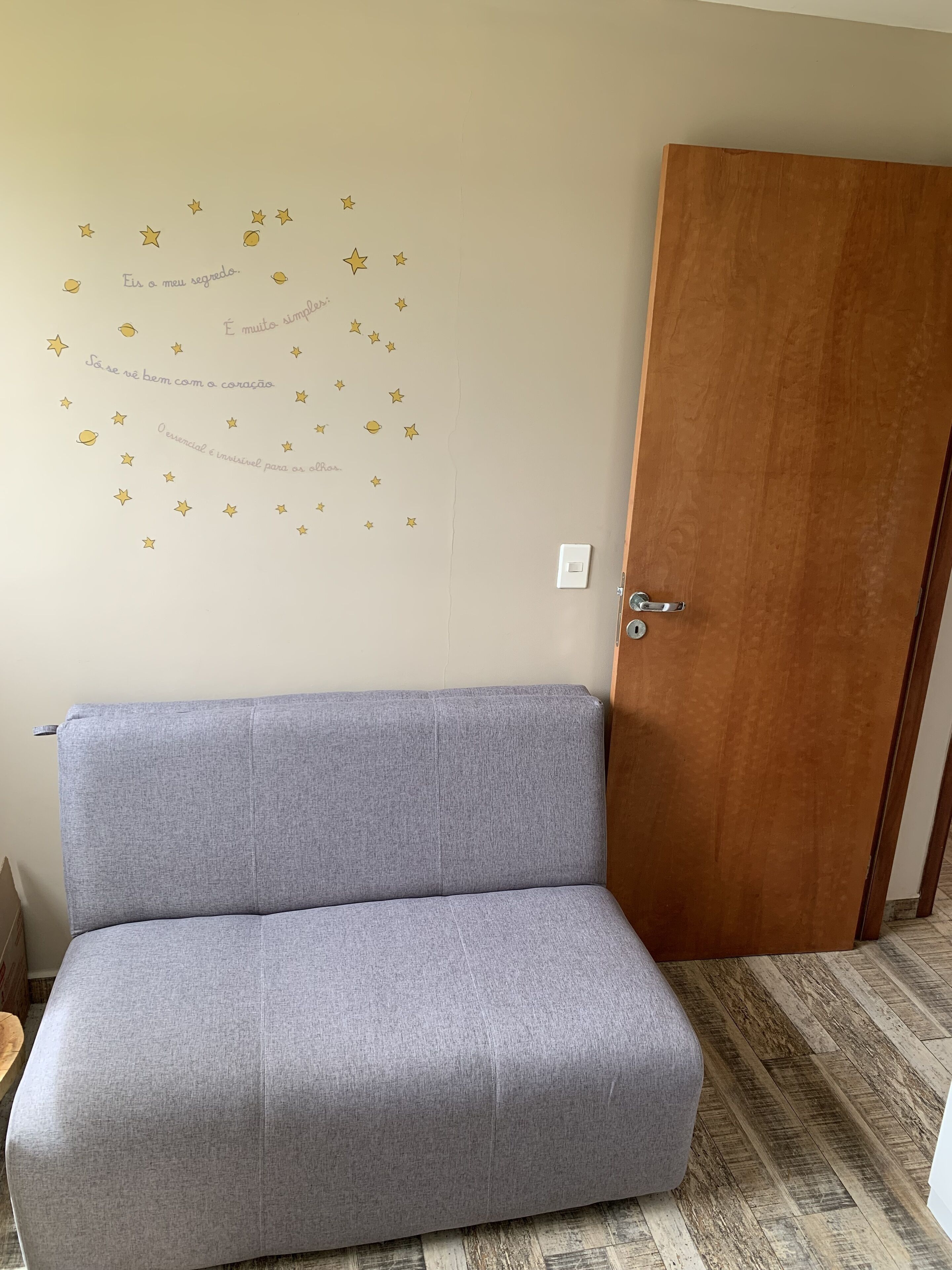 A room with a grey sofa, a wooden door, and a wall with star and moon decals.