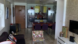 A modern living room with a sofa, chairs, a TV, and a kitchen in the background. - Paraíso Frente mar (Maceió)