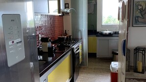 A modern kitchen with stainless steel appliances, a red-tiled backsplash, and a window providing natural light. - Paraíso Frente mar (Maceió)