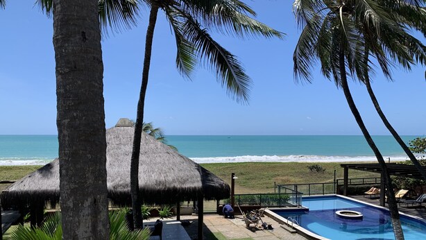 A pool area with a thatched-roof structure, a clear view of the ocean, and a well-maintained lawn. - Paraíso Frente mar (Maceió)