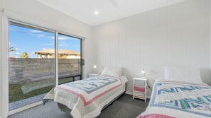 A bedroom with two beds, a sliding glass door to a balcony, and a view of a building outside.