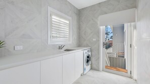 A modern kitchen with a built-in washing machine, a window with blinds, and a view to an outdoor balcony.