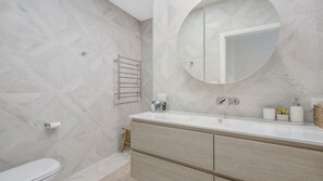 Een moderne badkamer met een witte wastafel, een ronde spiegel en een handdoekrek.