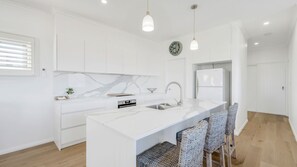 A modern kitchen with white cabinetry, a marble backsplash, a built-in island with bar stools, and a refrigerator.