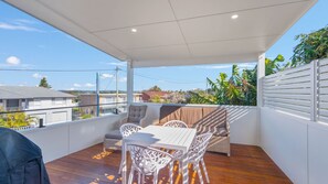Een overdekt terras buiten met een tafel, stoelen en uitzicht op de omgeving, met een houten vloer.