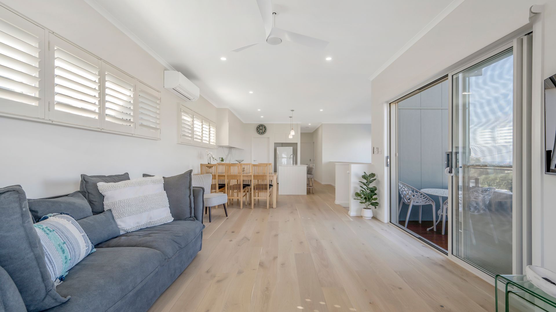A modern living room with a grey sofa, a dining area with a wooden table, and a kitchen in the background.