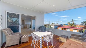Een balkon met een tafel en stoelen, een overdekte barbecue en uitzicht op de omgeving.