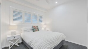 Een slaapkamer met een bed, twee nachtkastjes en een raam met zonwering.