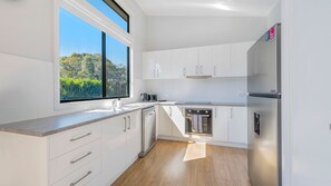 Une cuisine moderne avec des meubles blancs, un réfrigérateur en acier inoxydable et une fenêtre donnant sur un espace verdoyant.
