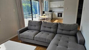 A modern living room with a grey sectional sofa, a white coffee table, and a view of a kitchen and balcony.