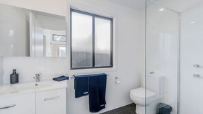 A modern bathroom with a white sink, a mirror, a window, a toilet, and a shower area. - Coastal Charm - Tastefully furnished holiday house (Port Macquarie)