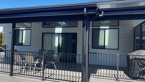 Een modern gebouw met een overdekt terras, grote ramen en een metalen hek.