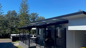 A modern building with a covered outdoor area, a garage, and a large tree in the background. - Coastal Charm - Tastefully furnished holiday house (Port Macquarie)