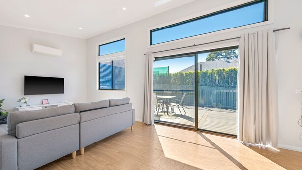 Een moderne woonkamer met een grijze bank, een flatscreen televisie en een schuifdeur die leidt naar een terras.