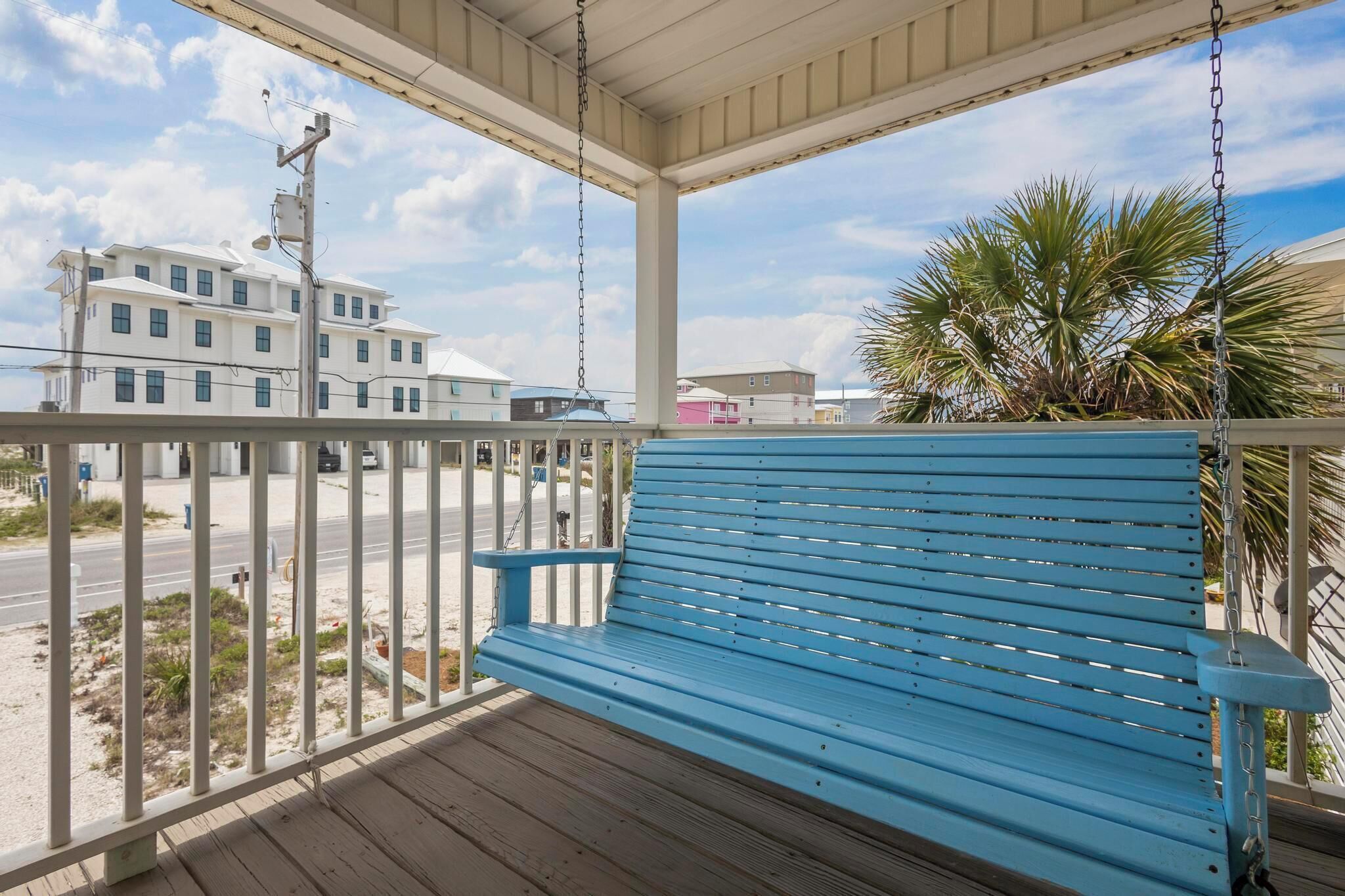 A blue bench on a wooden deck with a view of a building and palm trees.