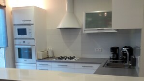 A modern kitchen with white cabinets, a built-in oven, a microwave, a gas stove, and a coffee maker.
