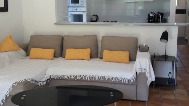 A modern living room with a sofa, a coffee table, and a kitchen area in the background.
